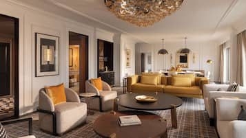 A well-lit, spacious living area with a modern chandelier, a sofa set, and a dining area with a view of the kitchen.