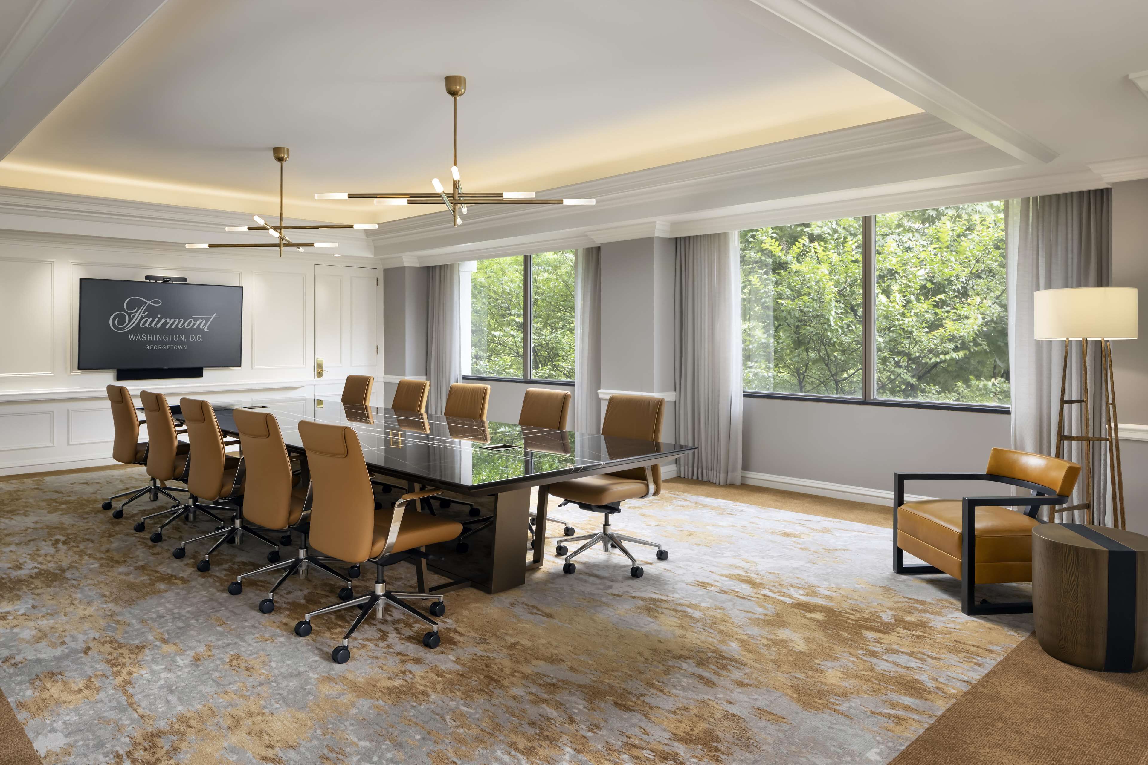 Une salle de conférence dotée d’une table en verre, de fauteuils en cuir, d’un téléviseur à écran plat et de grandes fenêtres.
