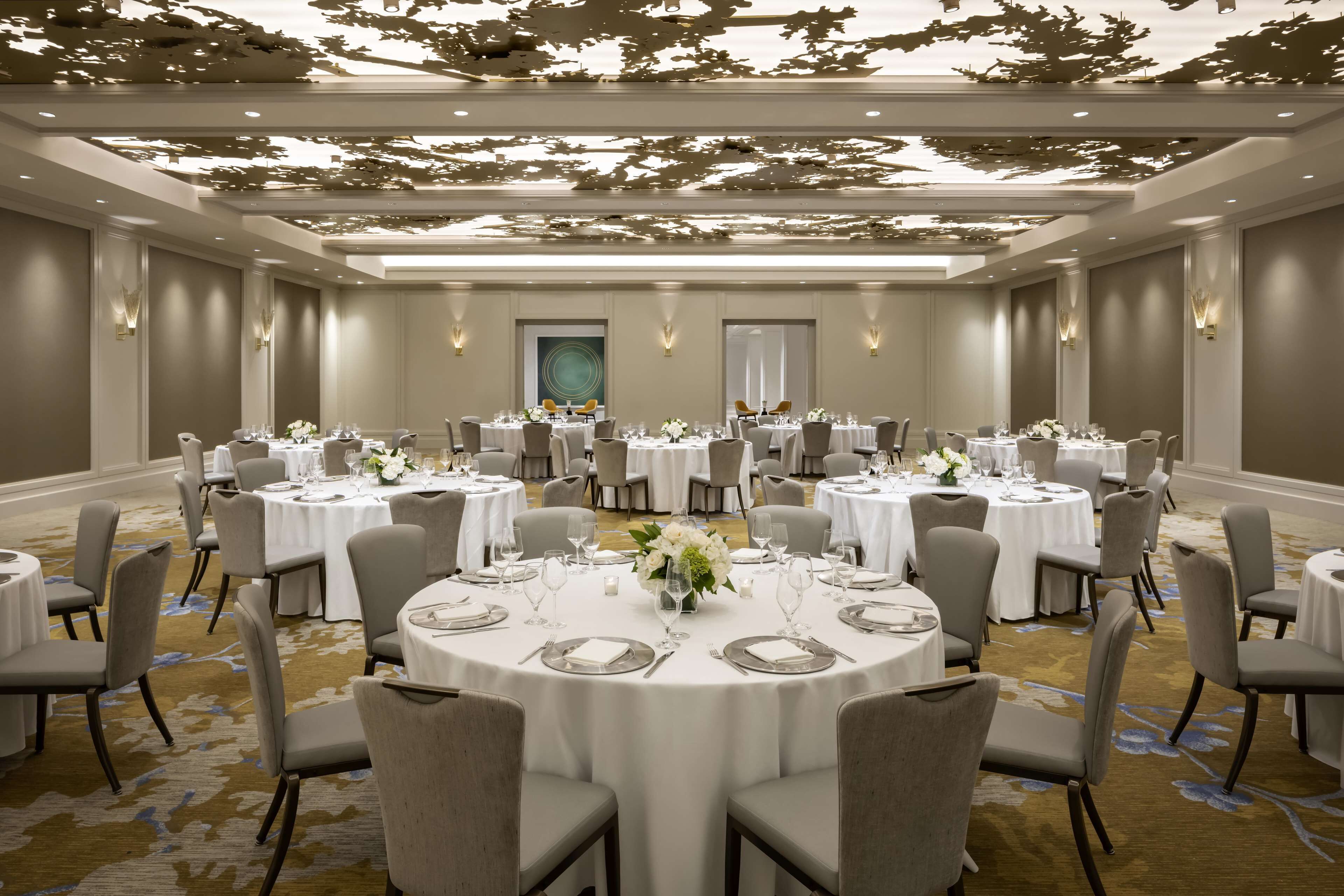 A banquet hall with round tables set for dining, featuring white tablecloths and floral centerpieces.