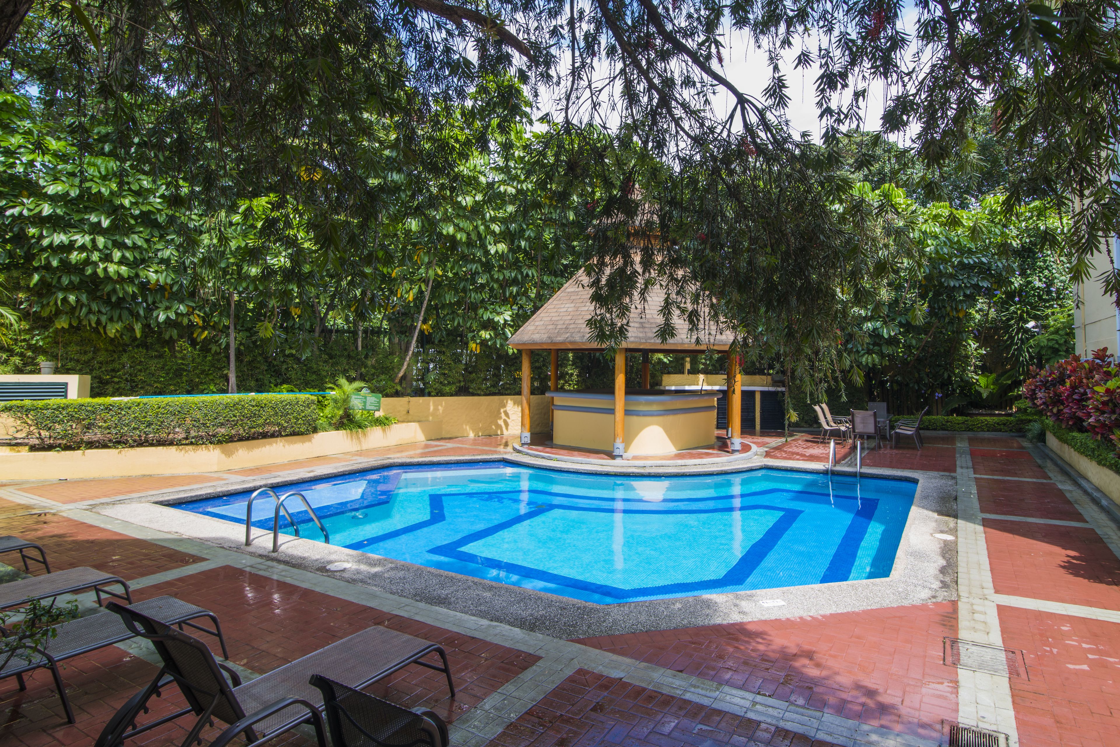 A rectangular swimming pool with a wooden gazebo and lounge chairs in a landscaped garden.