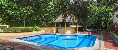 A rectangular swimming pool with a wooden gazebo and lounge chairs in a landscaped garden.