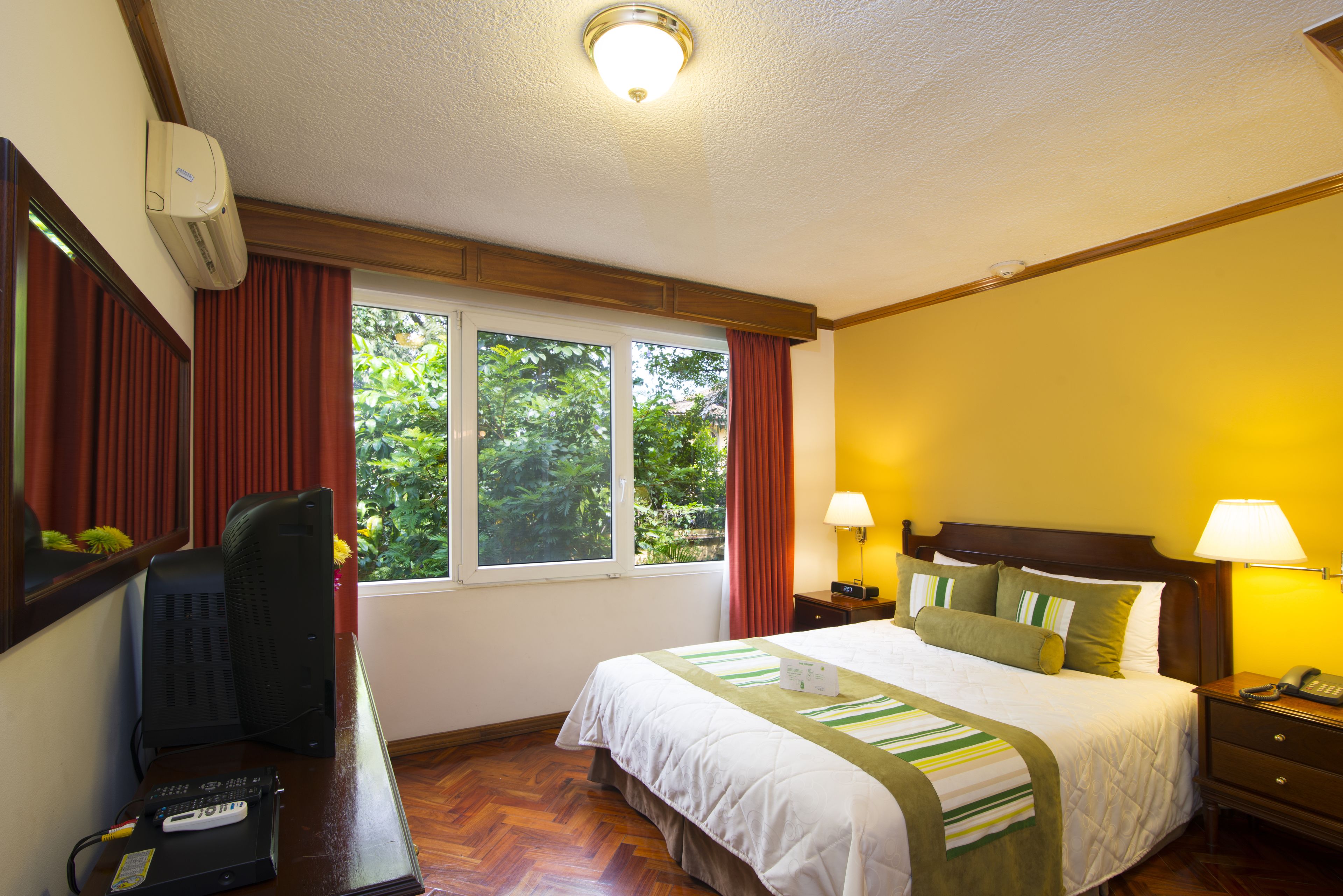 A hotel room with a bed, bedside lamps, a desk with a computer, and a window with curtains.