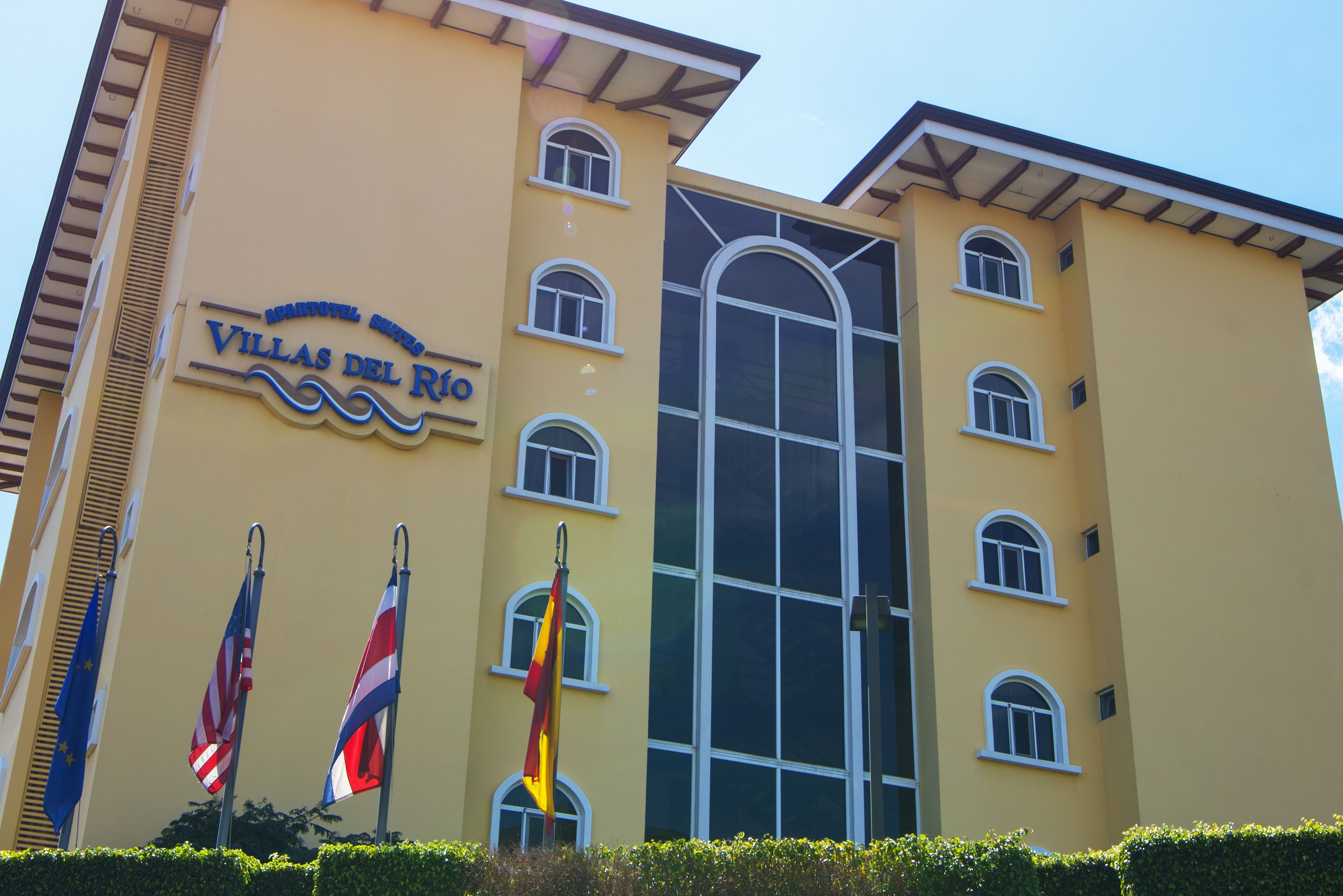 Un hôtel appelé « Villas del Rio », avec une façade jaune, de nombreuses fenêtres et des drapeaux.