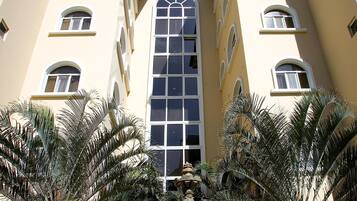 A building with a central arched window and multiple smaller windows, surrounded by palm trees and a fountain.
