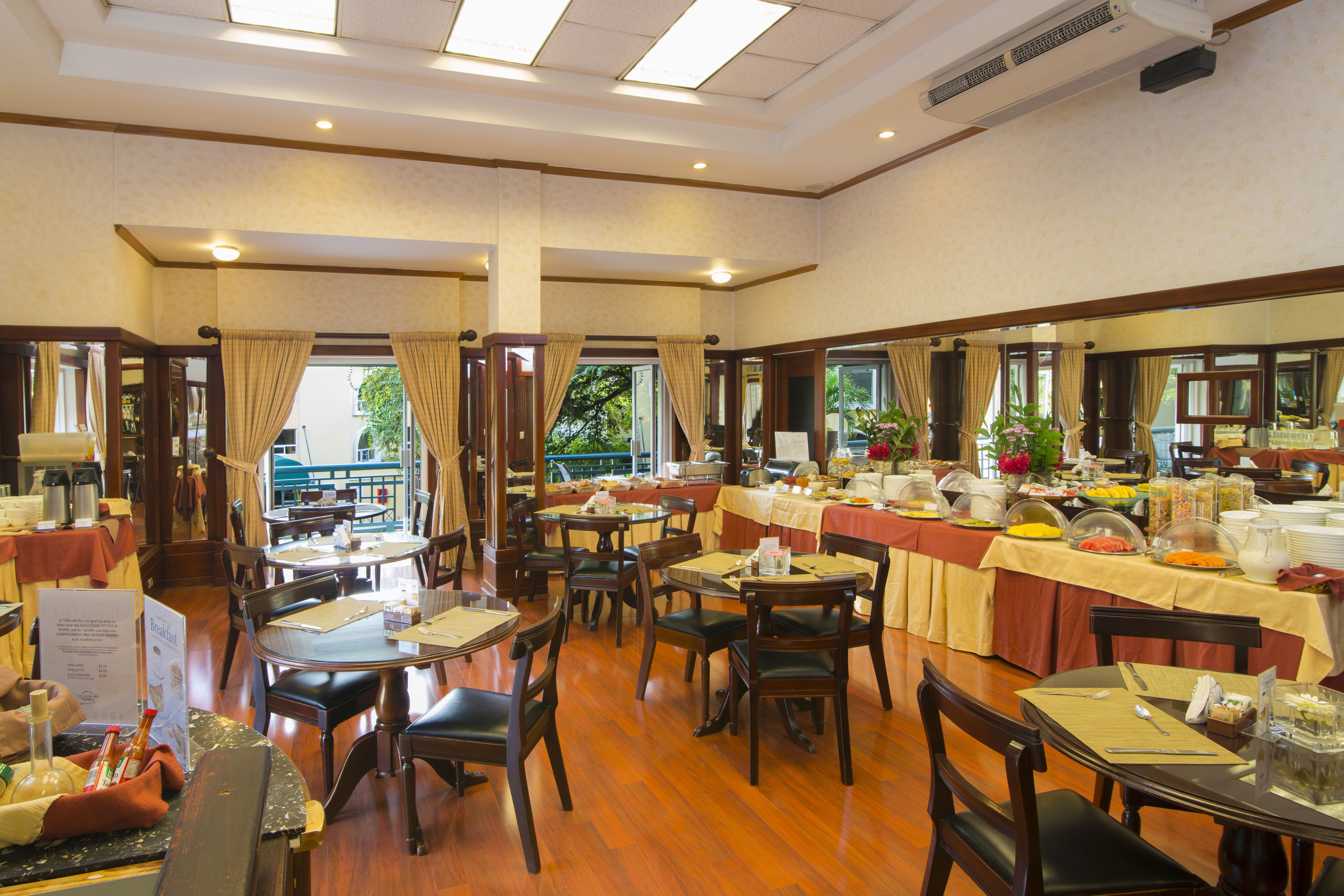 A dining area with multiple tables and chairs, a buffet setup, and a view of the outdoors.