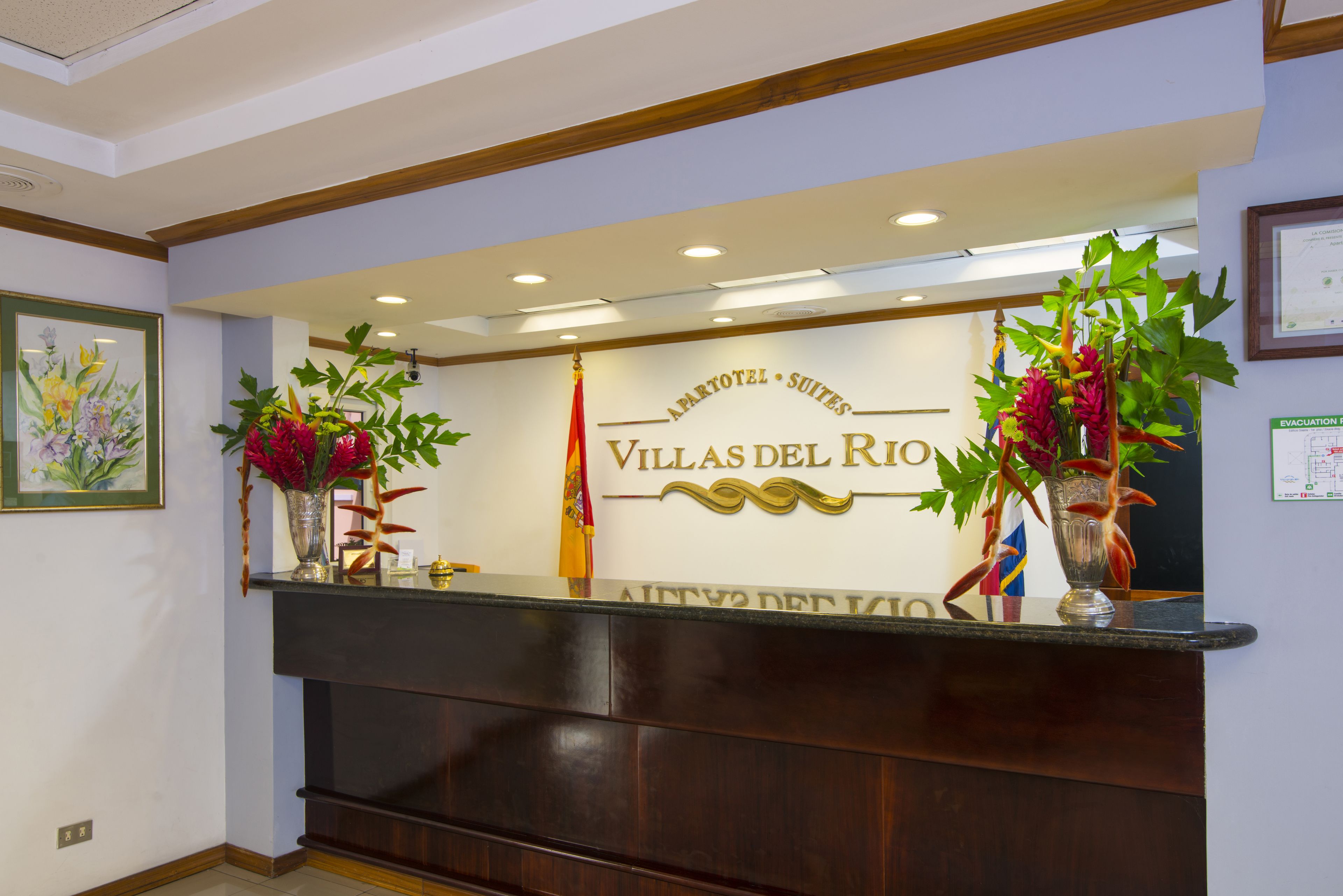 A reception desk with a sign reading "Villas del Rio" and two potted plants.