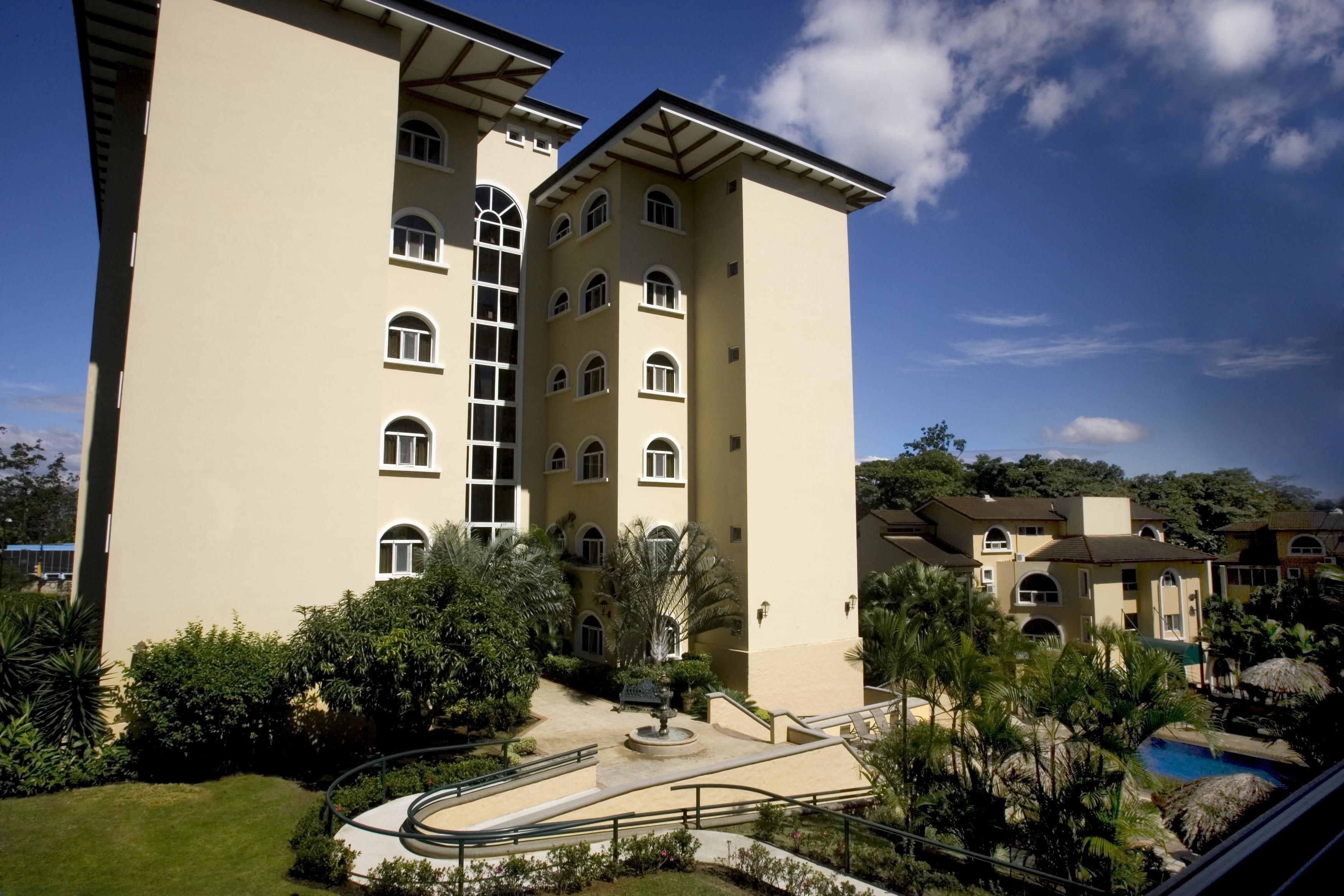 A multi-story hotel with a central courtyard, a swimming pool, and lush greenery.