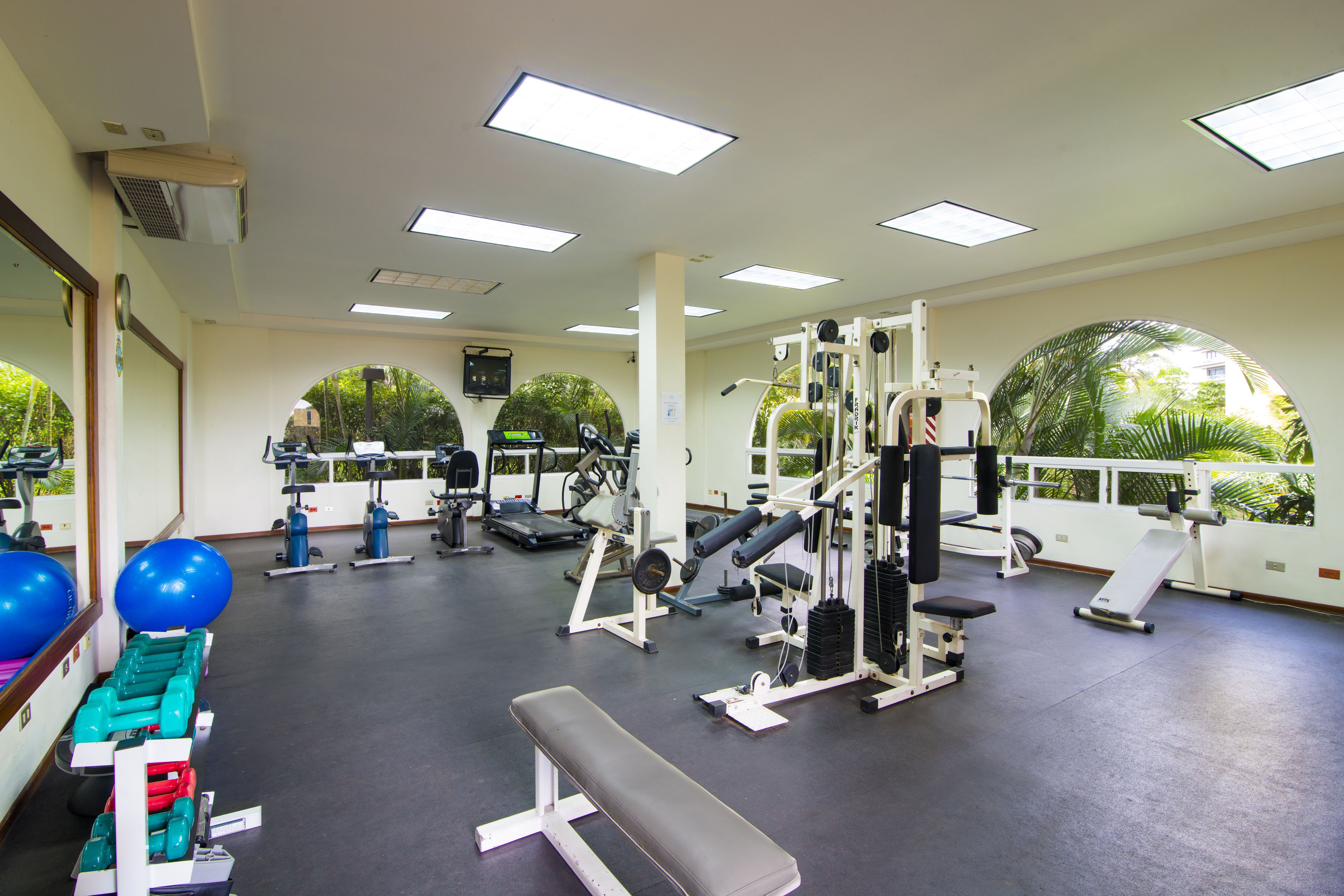 A gym with exercise equipment, a bench, and large windows with a view of greenery.