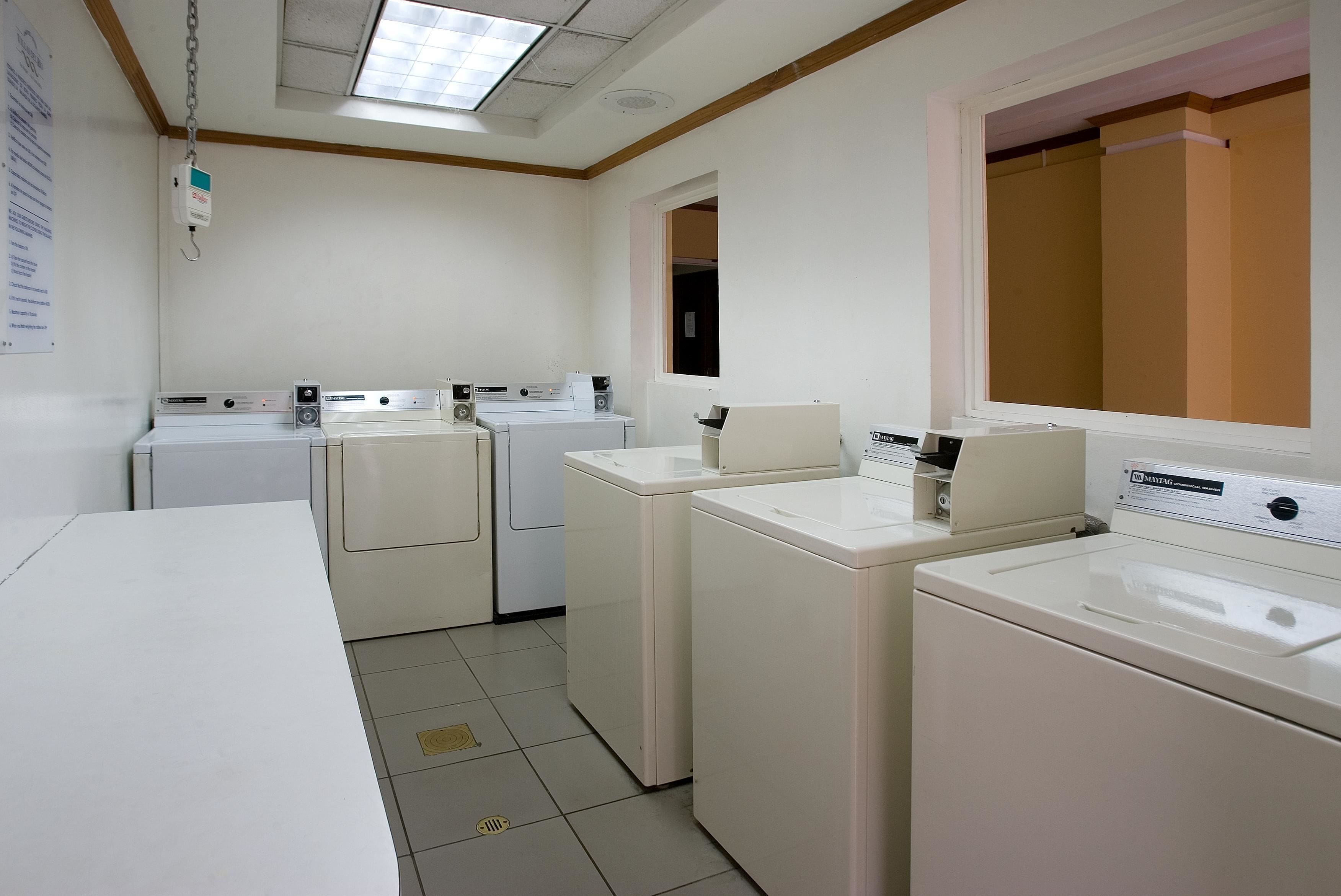 A laundry room with four white washing machines, a white sink, and a ceiling light fixture.