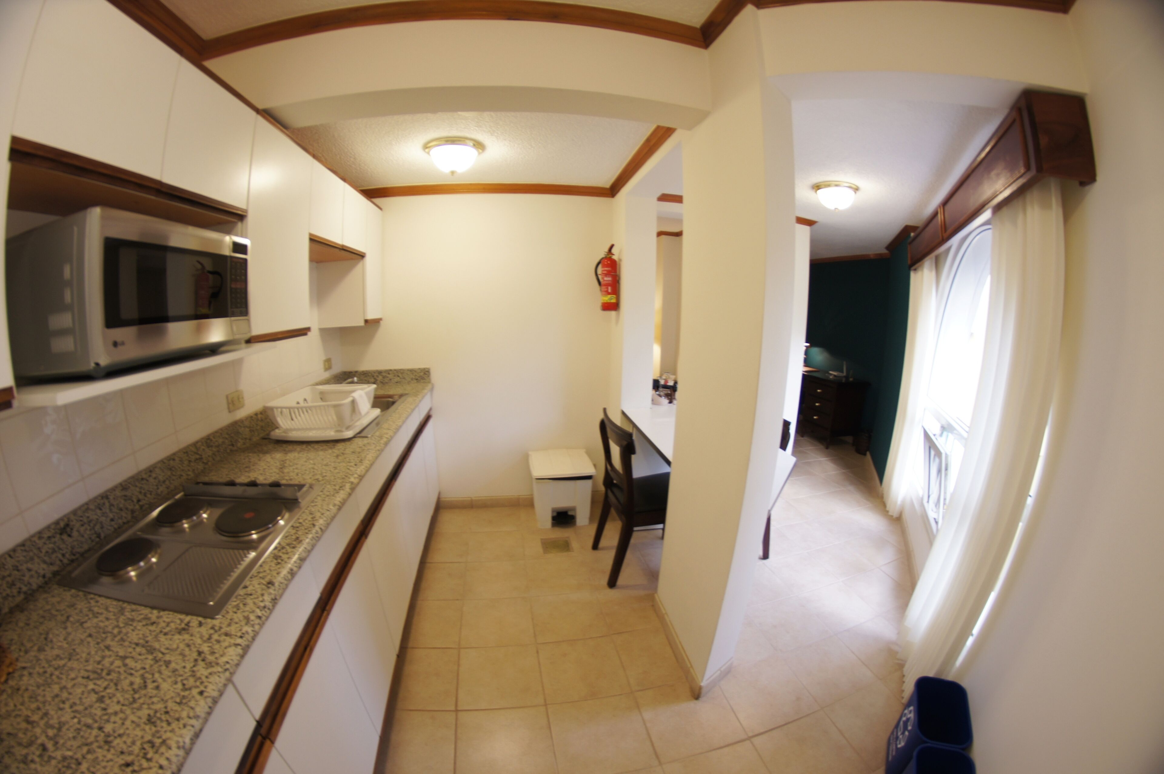 A kitchen with a microwave, stove, and sink. There is a small table and chair in the middle of the room.