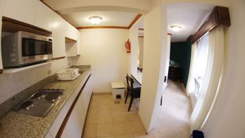 A kitchen with a microwave, stove, and sink. There is a small table and chair in the middle of the room.
