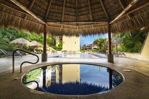 An infinity pool with a thatched roof, surrounded by lounge chairs and palm trees. - Apartotel & Suites Villas del Rio (San Rafael)