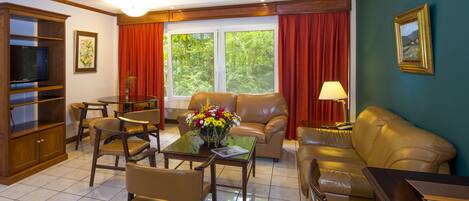 A living room with a sofa, chairs, a coffee table with flowers, a TV, and a painting on the wall.