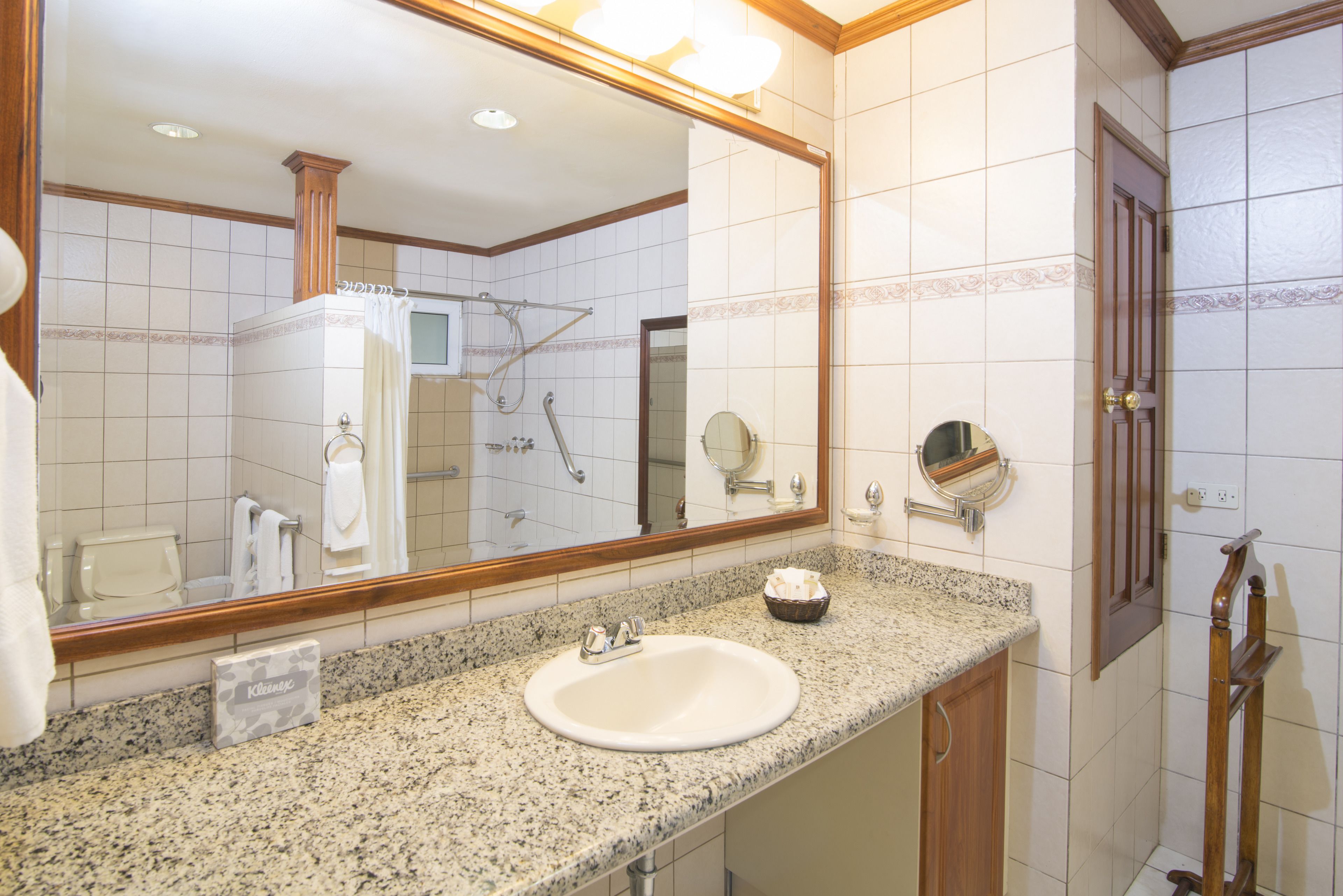 A bathroom with a granite countertop sink, a large mirror, a shower, and a wooden door.