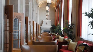 Un vestíbulo de hotel con sillones de cuero, un sofá rojo, una chimenea y una planta grande.