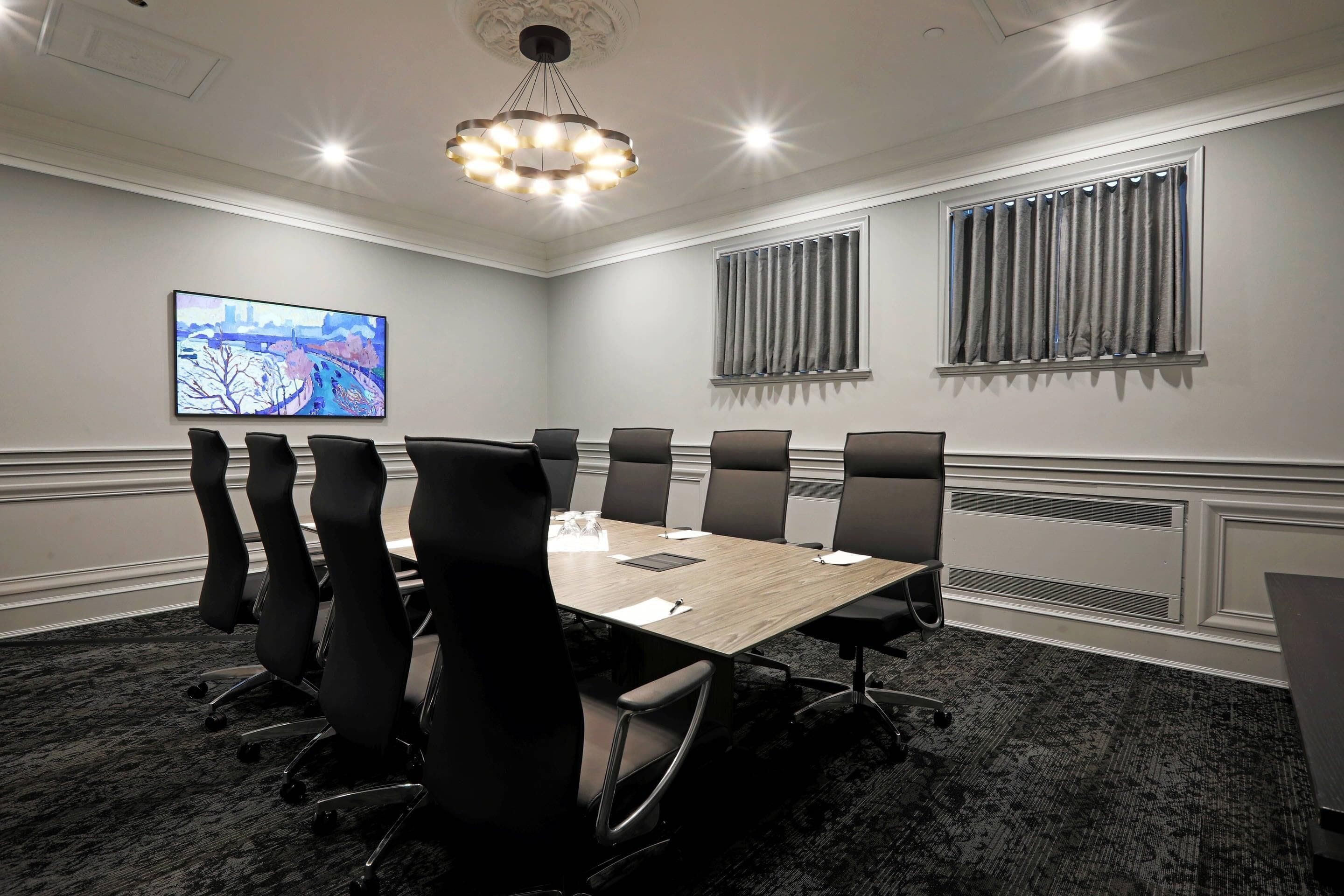 A conference room with a long table, black chairs, a projector screen, and a chandelier.