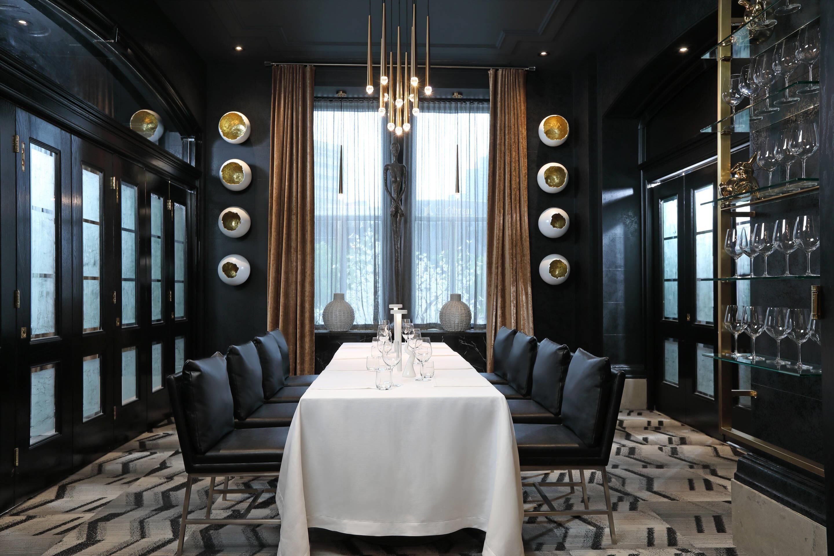 Ein formeller Speisesaal mit langem Tisch, schwarzen Ledersitzen und einem Chandelier.