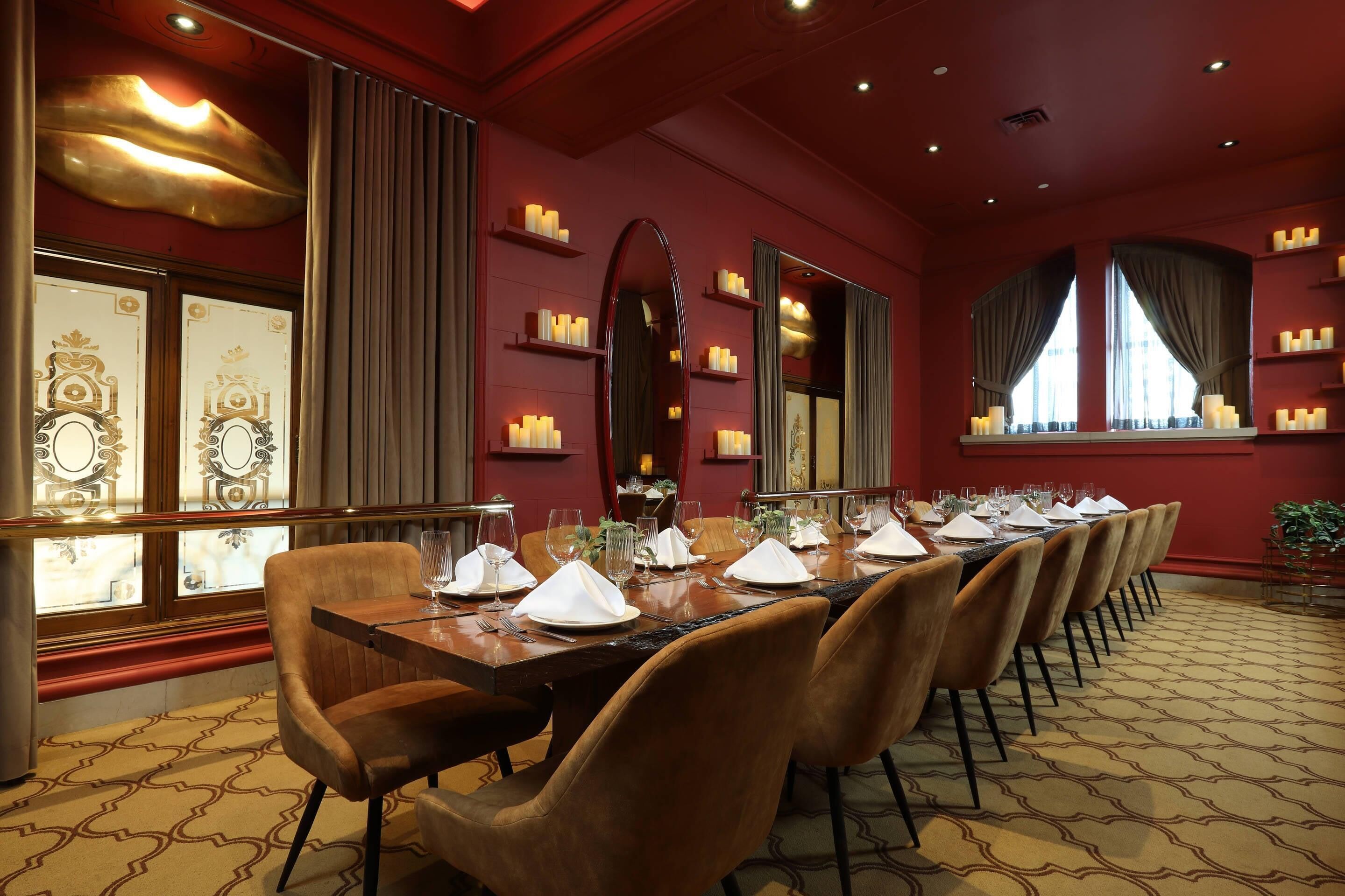 A long dining table set for a meal with chairs, candles, and a mirror on the wall.