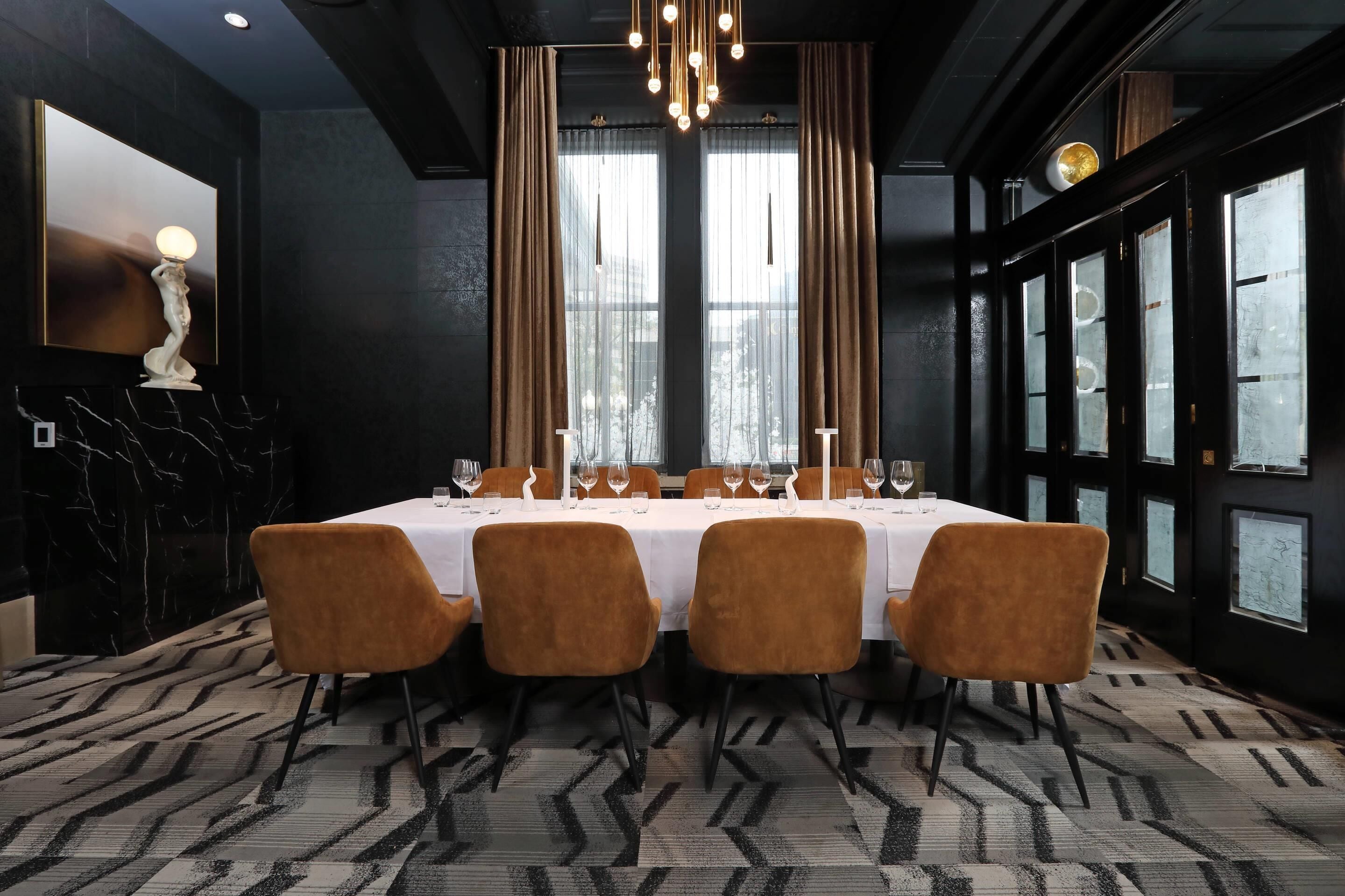 Un comedor con una larga mesa dispuesta para seis personas, rodeada por cuatro sillas, una alfombra estampada y una lámpara de araña.