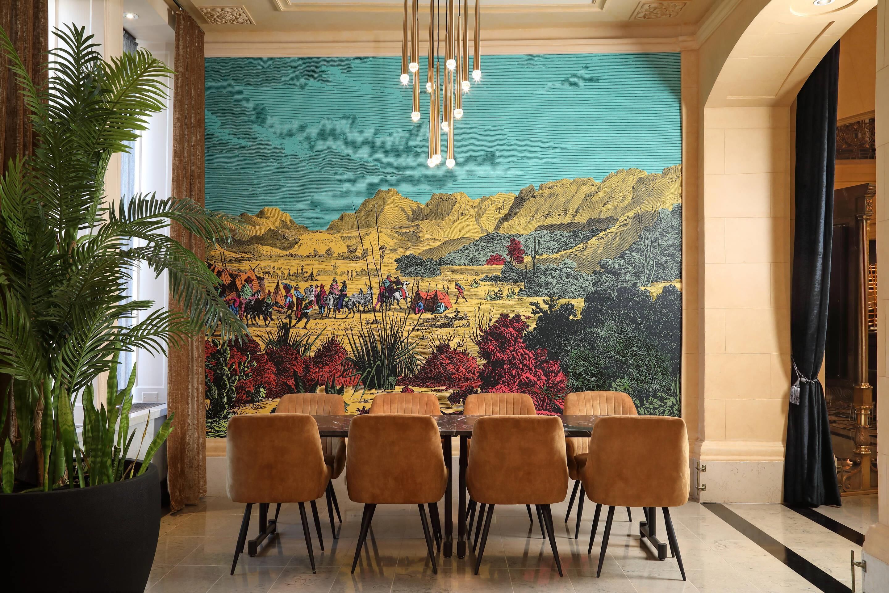 A dining area with a mural, a chandelier, and a large potted plant.