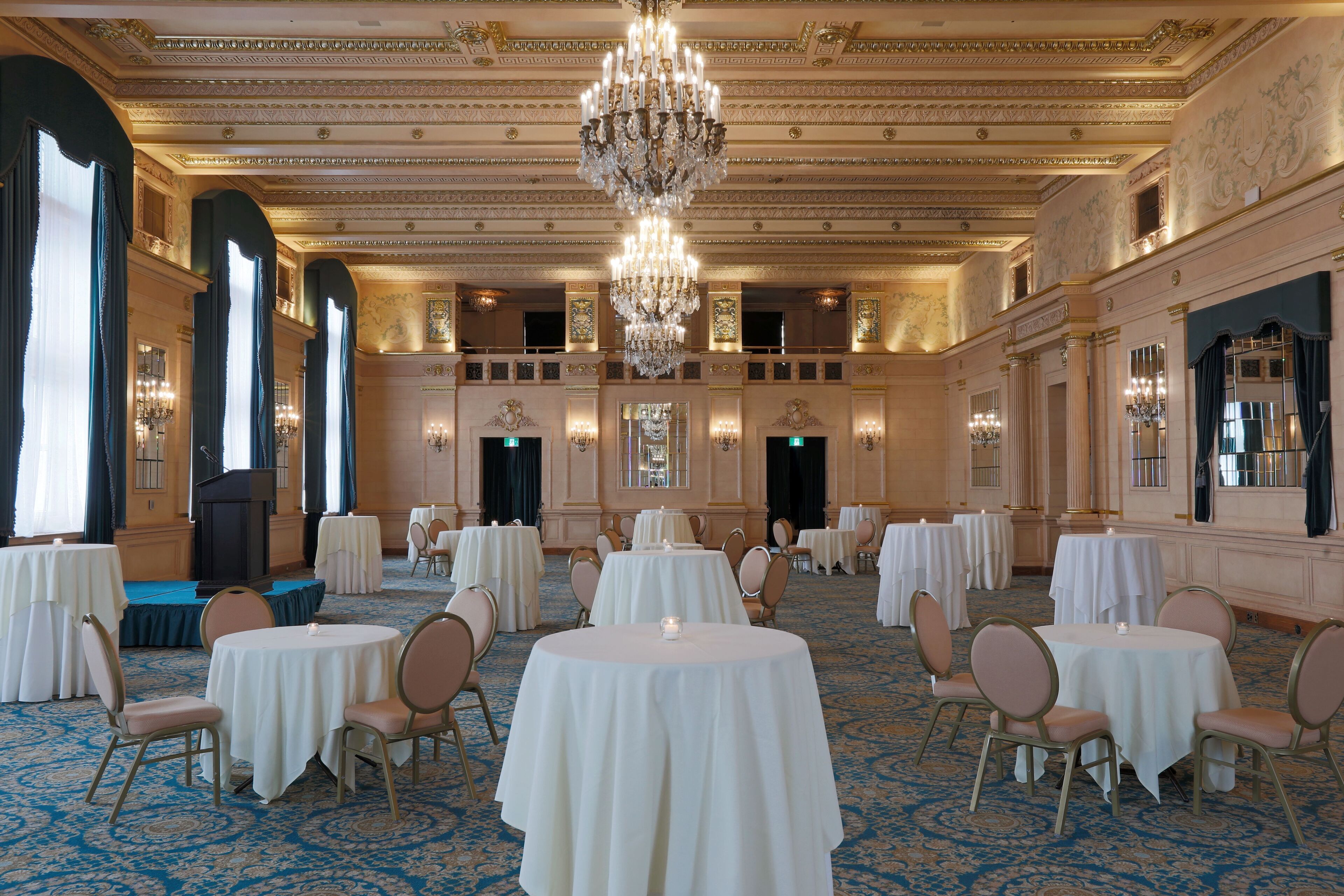 Una grande sala da ballo con numerosi tavoli rotondi, lampadari eleganti e architettura classica.