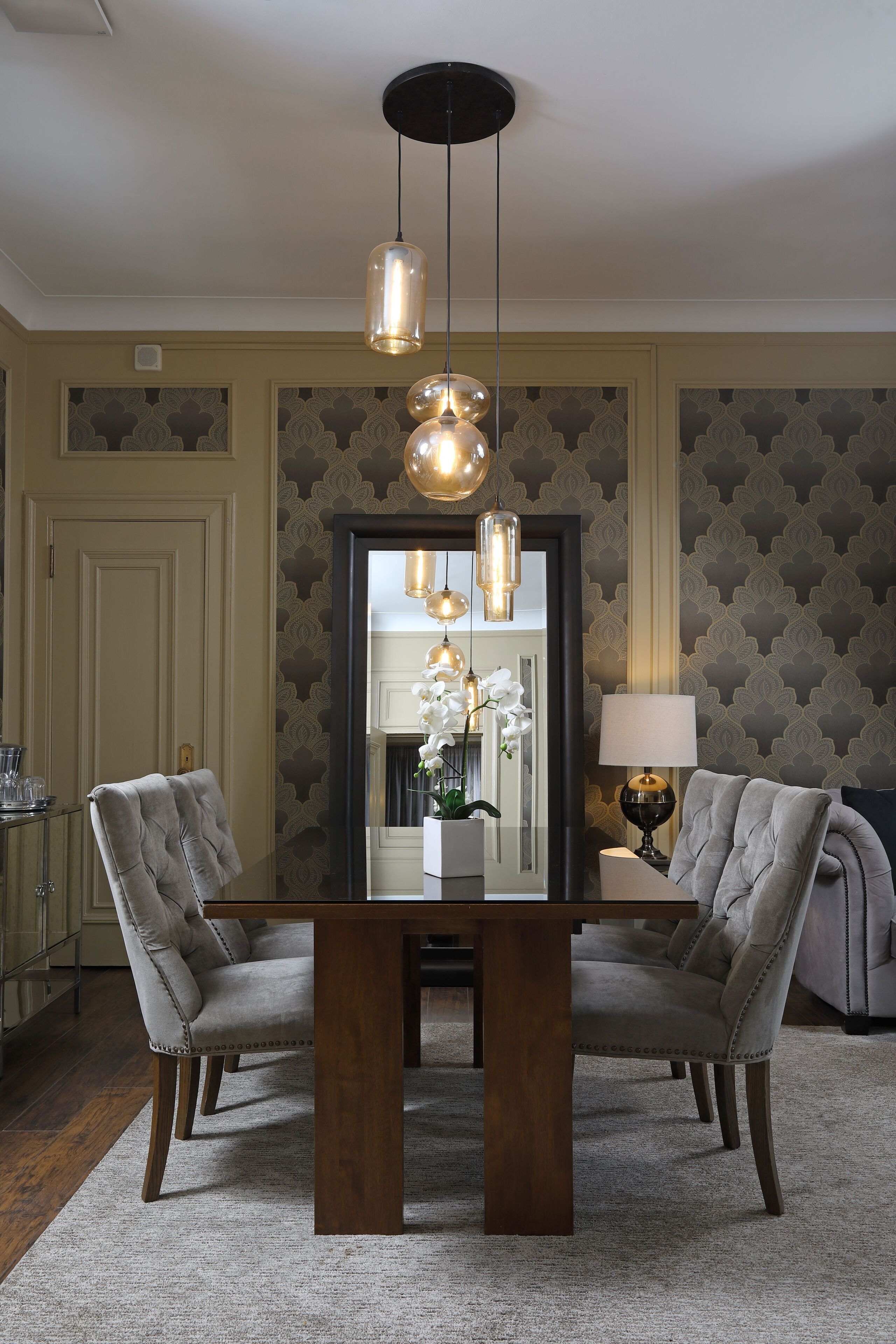 A dining area with a wooden table, two upholstered chairs, and pendant lighting.