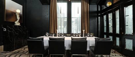 A dining area with a table set for four, black chairs, a chandelier, and large windows with curtains.