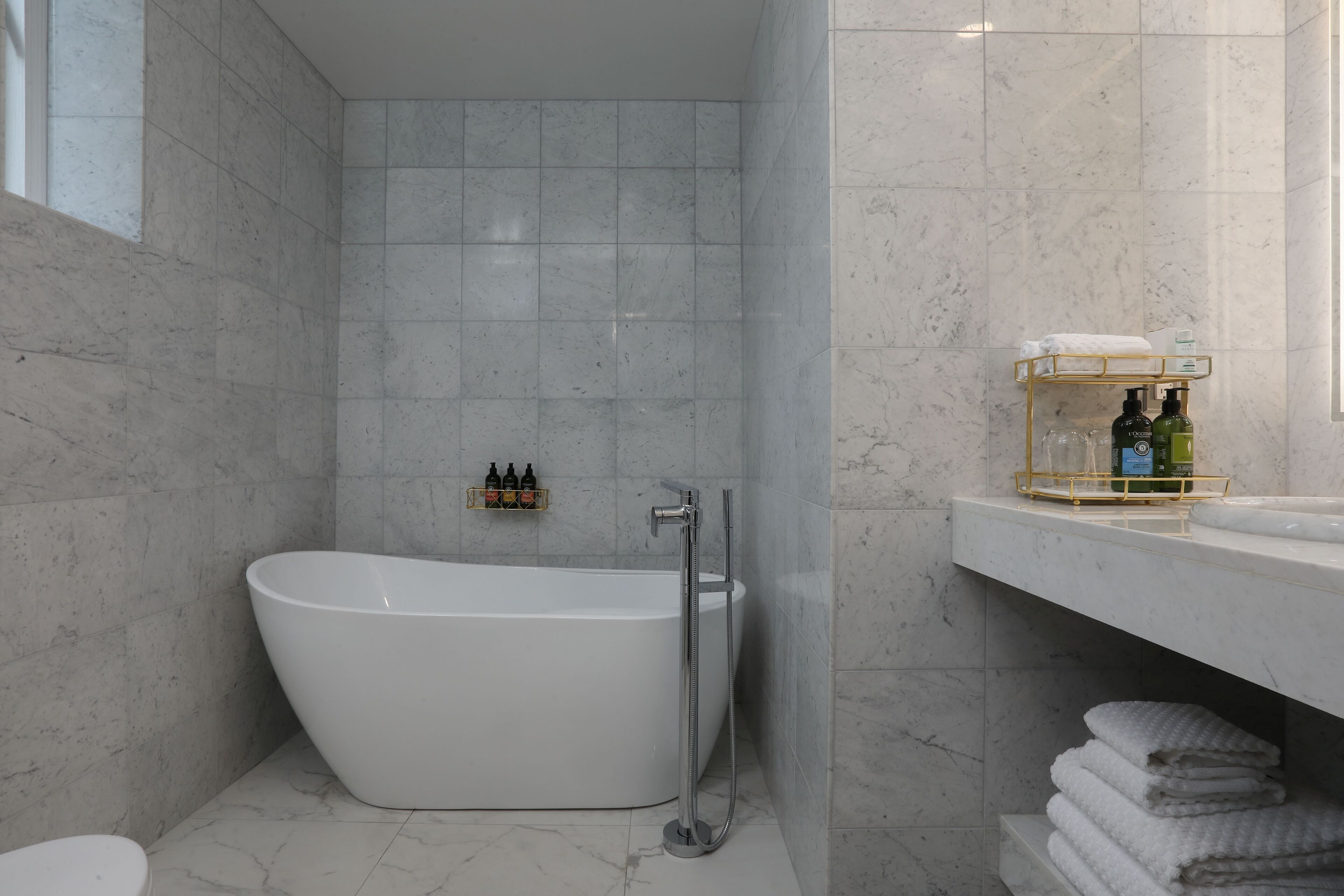A modern bathroom with a freestanding bathtub, a glass shower enclosure, and a marble-tiled wall.