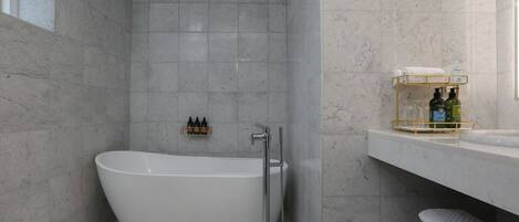 Un baño moderno con una bañera independiente, cabina de ducha con paredes de vidrio y un revestimiento de mármol.