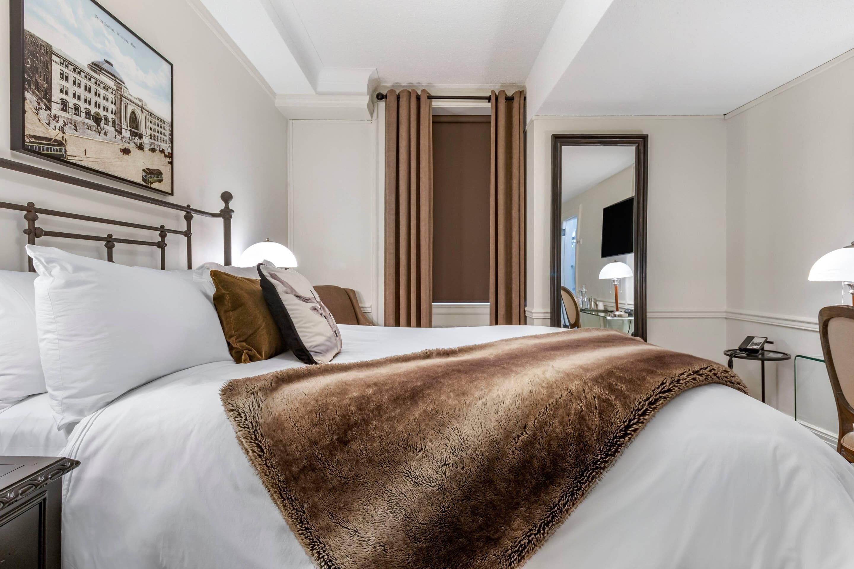 Habitación de hotel con una cama grande, cabecera, espejo, mesita de noche y un cuadro en la pared.