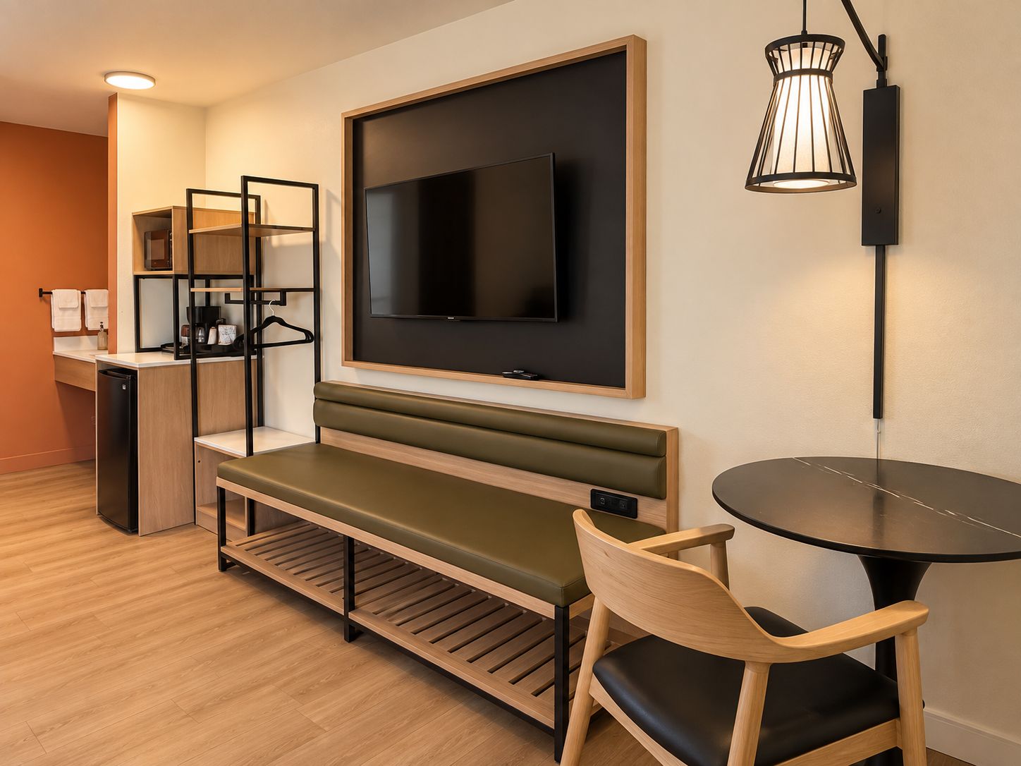 Une chambre d’hôtel moderne équipée d’un téléviseur à écran plat, d’un banc, d’une table à manger et d’une lampe fixée au mur.