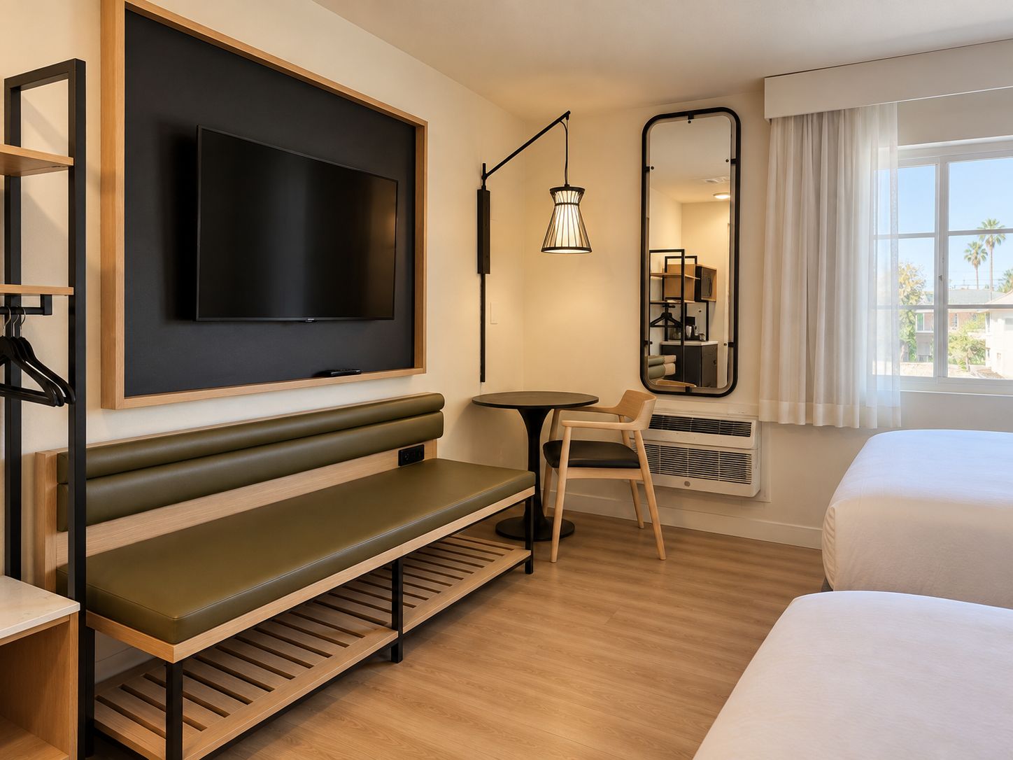 Habitación de hotel con cama, banca, mesa, silla, televisor, lámpara, espejo y ventana con cortinas.
