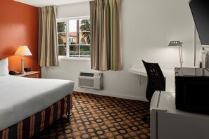 A hotel room with a bed, a desk, a chair, a lamp, a window, and an air conditioner.