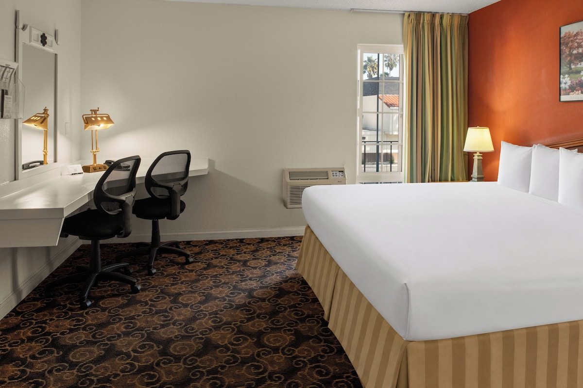 A hotel room with a bed, desk, chairs, and a window with curtains.