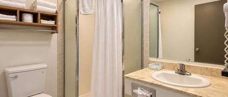 A bathroom with a glass-enclosed shower, a toilet, a sink, and a mirror with lights above.