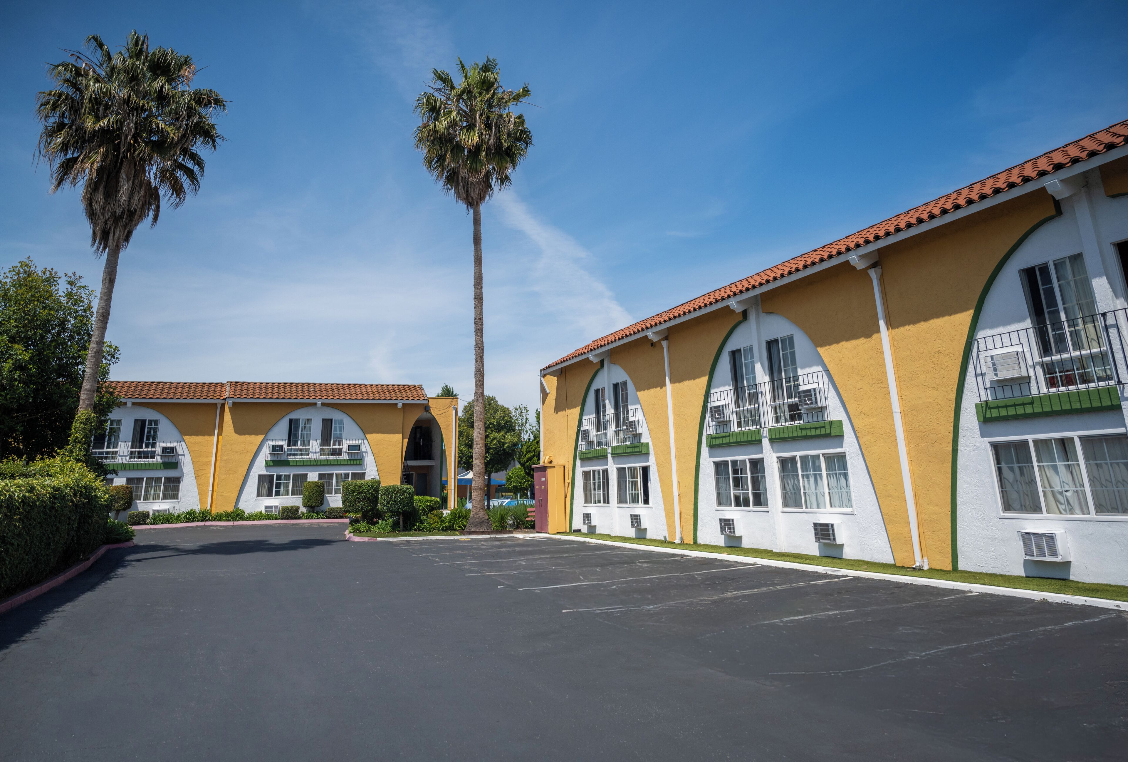 Un hôtel doté d’un parking, de deux palmiers et surplombant un ciel bleu azur.