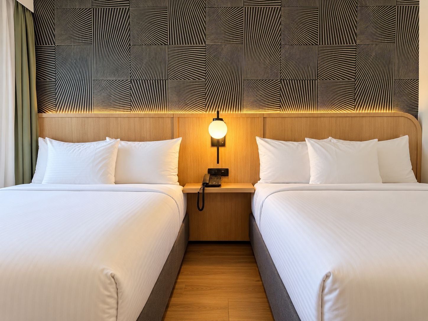 Quarto de hotel com duas camas, cabeceira de madeira, luz acoplada à parede e telefone.