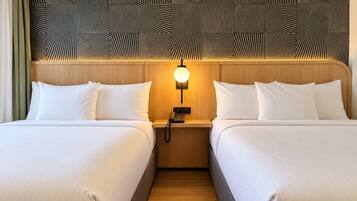 Quarto de hotel com duas camas, cabeceira de madeira, luz acoplada à parede e telefone.