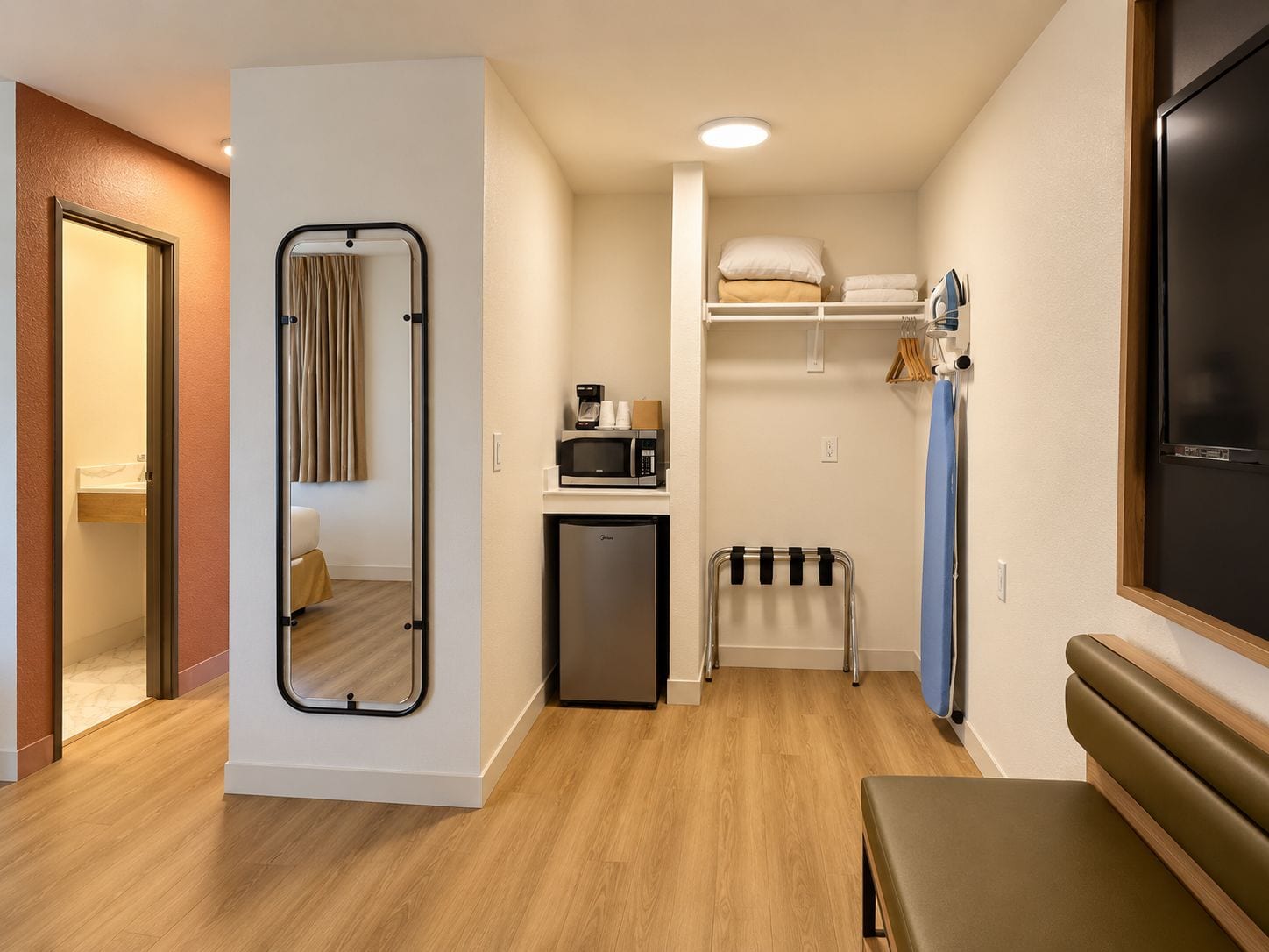 Habitación de hotel compacta con cama, kitchenette pequeño, espejo y zona de estar.