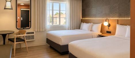 A hotel room with two beds, a desk, a chair, a mirror, and a window with curtains.