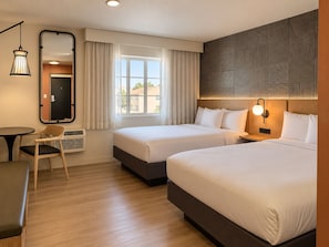 Une chambre d’hôtel avec deux lits, un bureau, une chaise, un miroir et une fenêtre avec des rideaux.