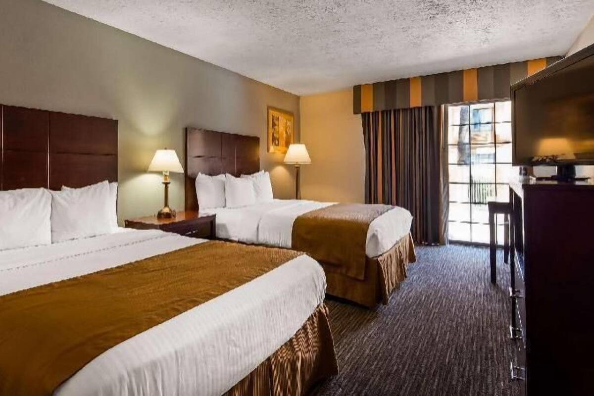 A hotel room with two beds, a desk, and a large window with curtains.