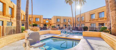 A pool area with a hot tub, palm trees, and a building with multiple windows.