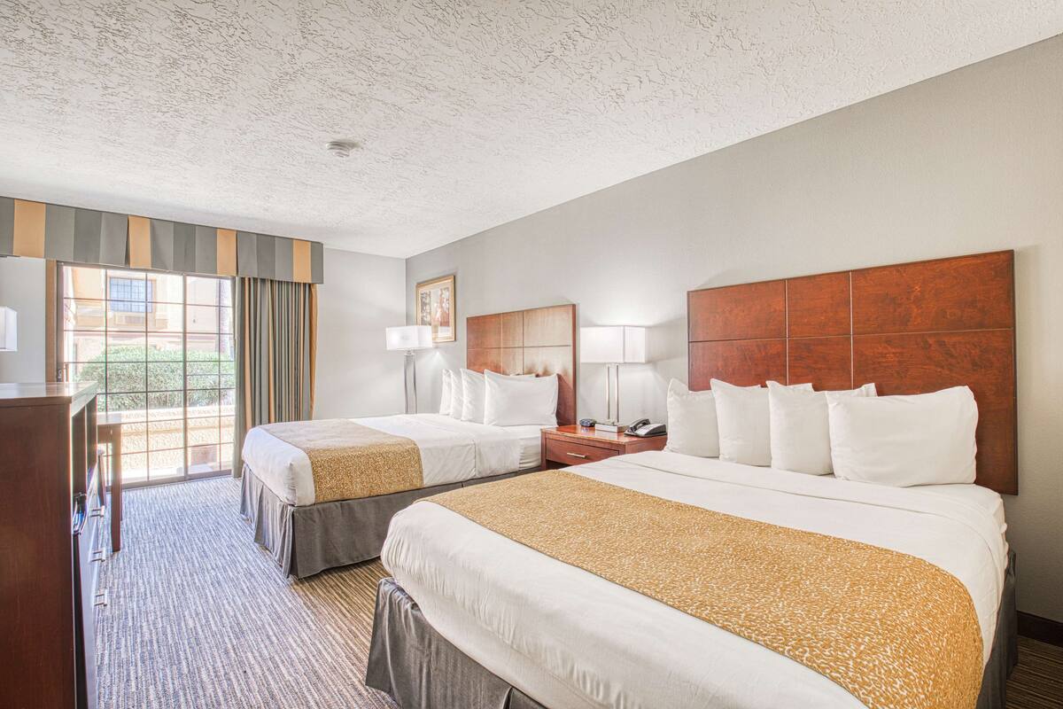 A hotel room with two beds, a desk, and a large window with curtains.