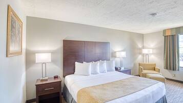 A hotel room with a large bed, two bedside tables with lamps, a chair, and a framed picture on the wall.