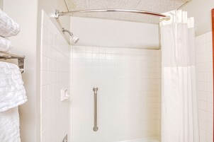 A bathroom with white tiled walls, a shower with a handheld showerhead, a grab bar, and a white shower curtain.