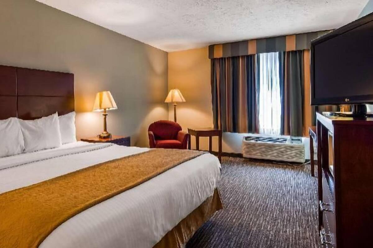A hotel room with a large bed, two bedside lamps, a red armchair, a small table, and a television.
