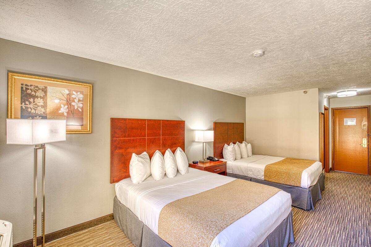 A hotel room with two beds, a large framed picture on the wall, a floor lamp, and a door.