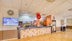 A hotel reception area with a reception desk, a large screen displaying hotel information, and a mural of a mountain landscape on the wall. - Best Western Green Valley Inn (Green Valley)