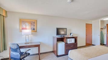 Quarto de hotel com uma cama, uma escrivaninha com cadeira, televisão, micro-ondas e um pequeno frigorífico.